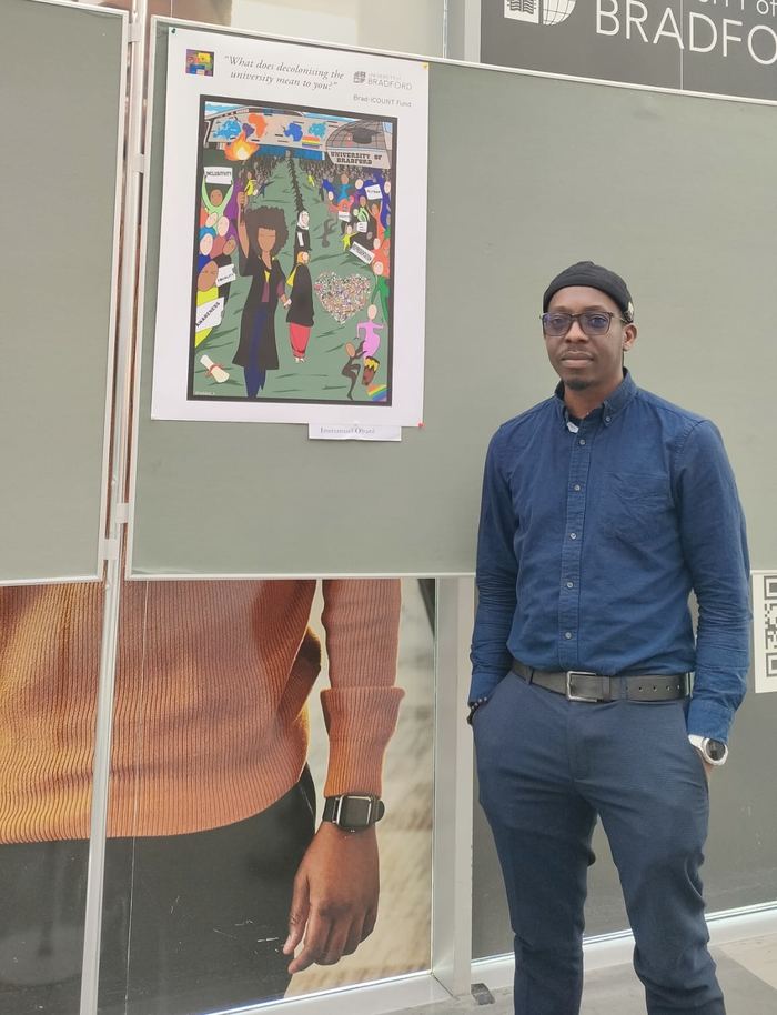 Immanuel Obani beside his artwork Decolonizing the University at the Brad-iCOUNT exhibition